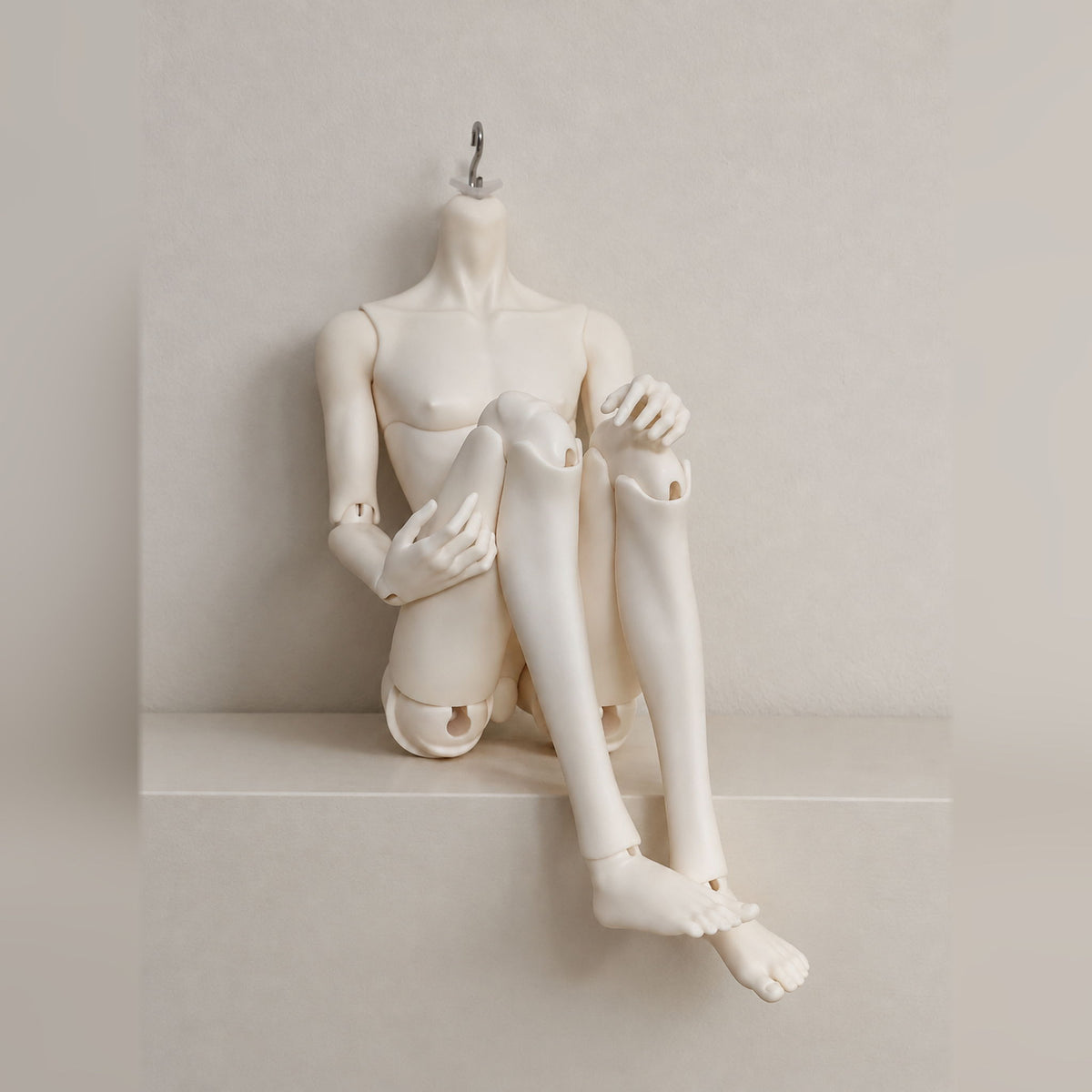 Articulated male BJD body in a compact seated pose with crossed legs