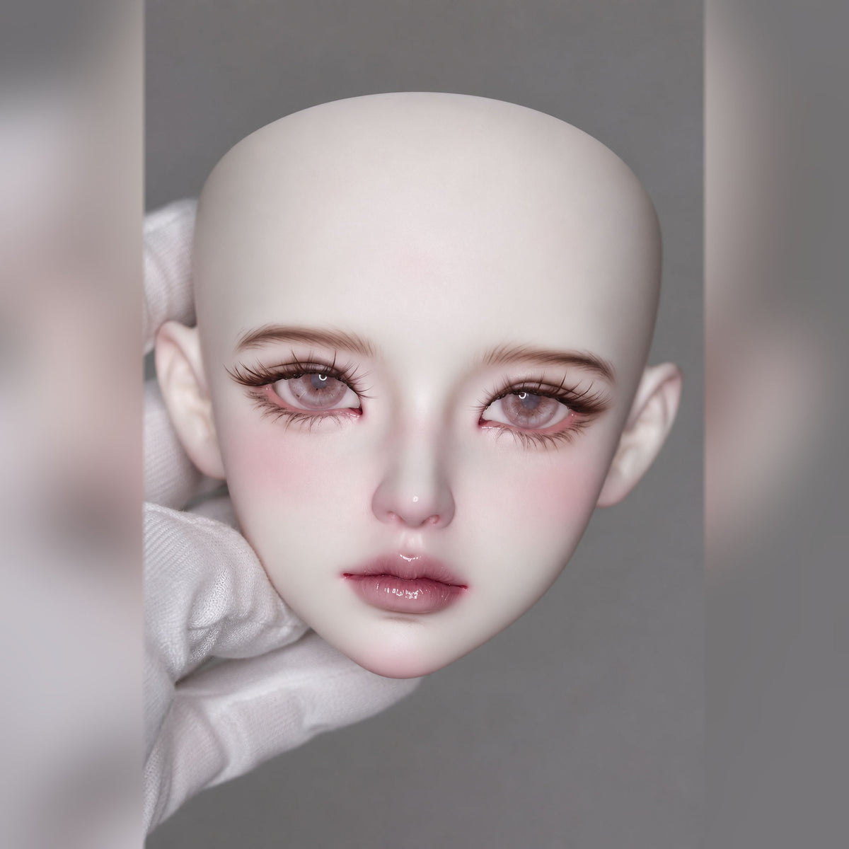 Front view of a female BJD head with long lashes, rosy eye makeup, pink eyes and glossy sculpted lips
