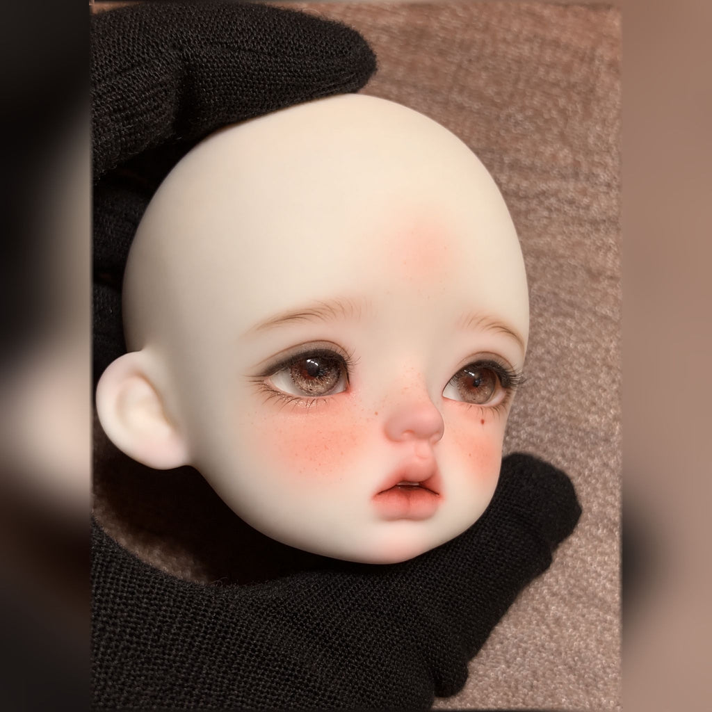 Three-quarter view of a girl BJD head with brown eyes, freckled cheeks and natural makeup