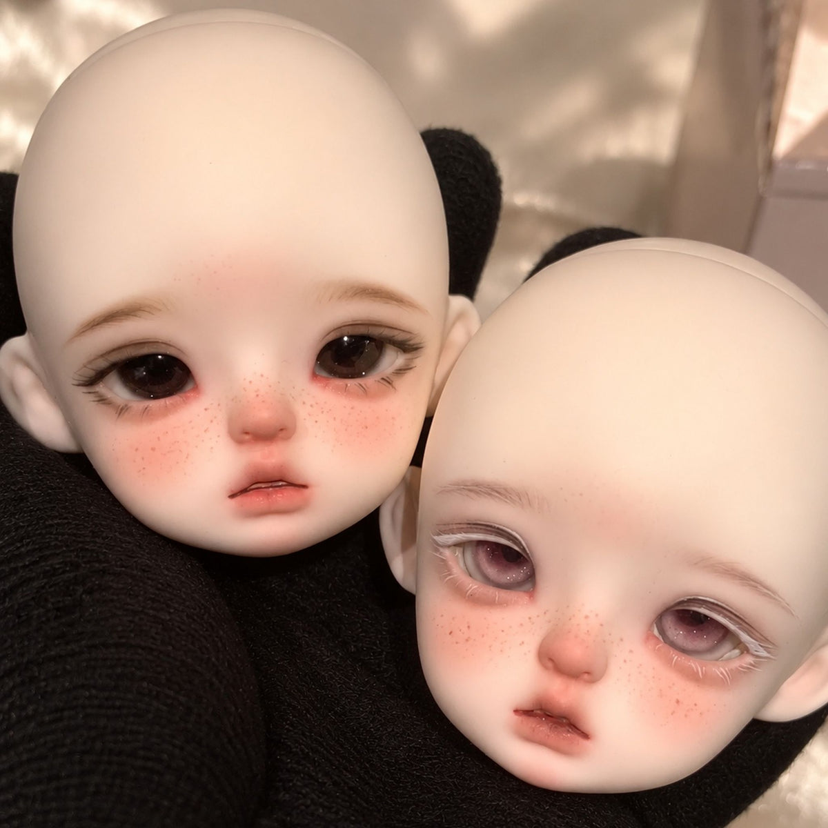 Two girl BJD heads displaying different freckled face-up styles and eye colors